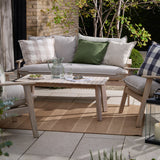 Chesil Check Printed Cotton Cushion in natural beige and off-white, styled with an oxford border on a grey outdoor sofa alongside plain and green scatter cushions.
