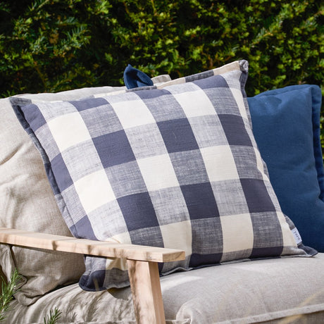 Chesil Check cotton cushion in navy and cream buffalo check, 50 x 50cm square, shown on a beige sofa outdoors alongside a plain navy cushion.