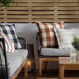 Chesil Check Printed Cotton Cushion in navy and cream buffalo check, styled on an outdoor sofa alongside striped and rust check cushions in a garden setting.