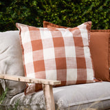 Chesil Check Printed Cotton Cushion in pecan brown and off-white gingham with flat edge trim, styled on a linen outdoor sofa beside a plain terracotta cushion.