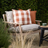 Chesil Check Printed Cotton Cushion in pecan brown and off-white gingham with flat trim, shown on a wooden outdoor sofa alongside plain grey and terracotta cushions.