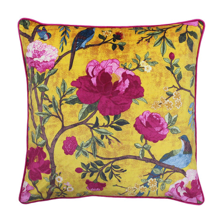 Square velvet cushion in gold with a chinoiserie print of pink and magenta flowers, branches and two blue birds, finished with a pink piped edge on a white background.