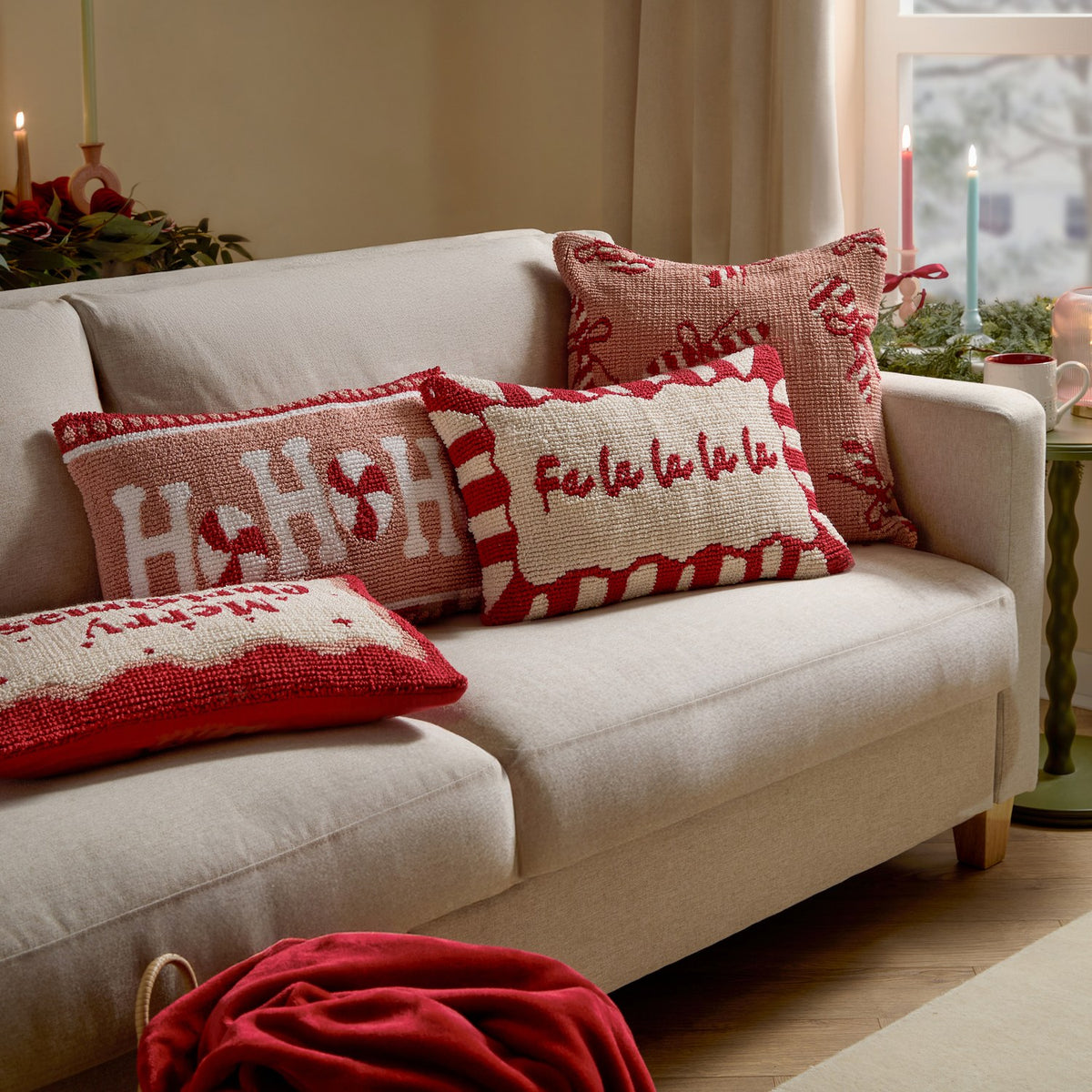 Candy Ho Ho Ho tufted cushion in pink and red with peppermint swirl design, styled on a beige sofa alongside matching festive cushions in a living room setting.