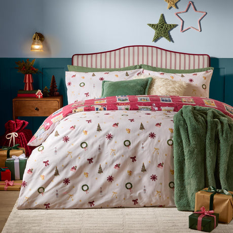 Cranberry cotton reversible duvet set with festive cream side and townhouse-print pink reverse, styled on a bed with green cushions and throw.