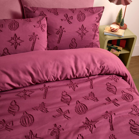 Berry-purple polyester duvet cover set with tonal tufted Christmas motifs of baubles, stars, bows and candy sticks, shown on a bed beside a nightstand with festive decor.