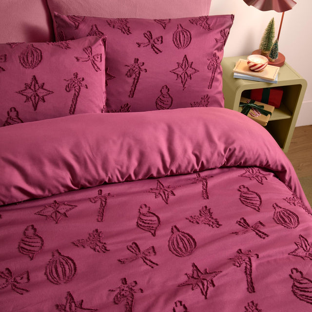 Berry-purple polyester duvet cover set with tonal tufted Christmas motifs of baubles, stars, bows and candy sticks, shown on a bed beside a nightstand with festive decor.