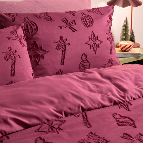 Berry-purple polyester duvet cover set with tonal tufted Christmas motifs, including baubles, stars and bows, styled on a bed in a bedroom setting.