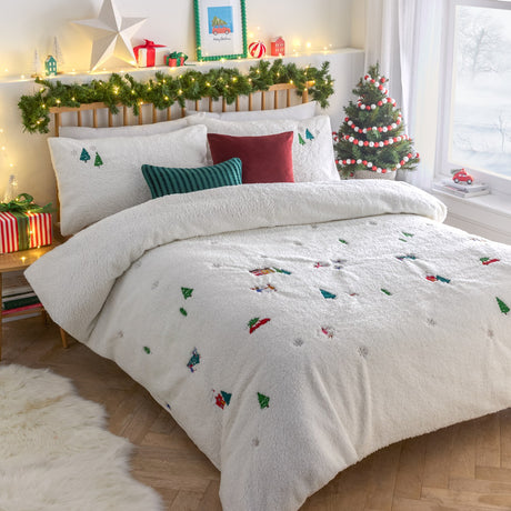 Cream fleece Christmas Together duvet cover set with embroidered trees, gingerbread house and snowman motifs, styled on a bed in a festive bedroom with cushions and tree.