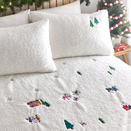 Christmas Together fleece duvet cover set in off-white, styled on a bed with matching pillowcases embroidered with trees, a gingerbread house, snowmen and snow angels.
