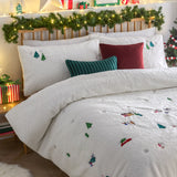 Christmas Together fleece duvet cover set in cream, styled on a bed with embroidered trees, snowmen and festive figures, paired with striped and plain cushions in a decorated bedroom.