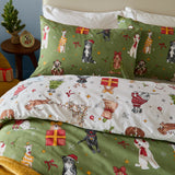 Christmas Pawty reversible cotton-blend duvet cover set on a bed, showing green side with festive dog prints and cream side with matching pattern on pillowcases.