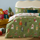 Christmas Pawty Cotton Reversible Duvet Cover Set in green, styled on a bed with matching pillowcases showing festive dogs, gifts, bows and stars, cream reverse peeking at the fold.
