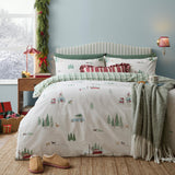 Christmas Tree Lane Check Duvet Cover Set in natural/sage, cotton bedding with a printed winter scene of cars, sleds and pine trees, styled on a bed with checked pillows in a festive bedroom.