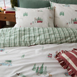 Christmas Tree Lane Duvet Cover Set in Natural/Sage, shown on a bed with pillowcases printed with cars, trees and deer, reverse side in green check, styled with a striped cushion.