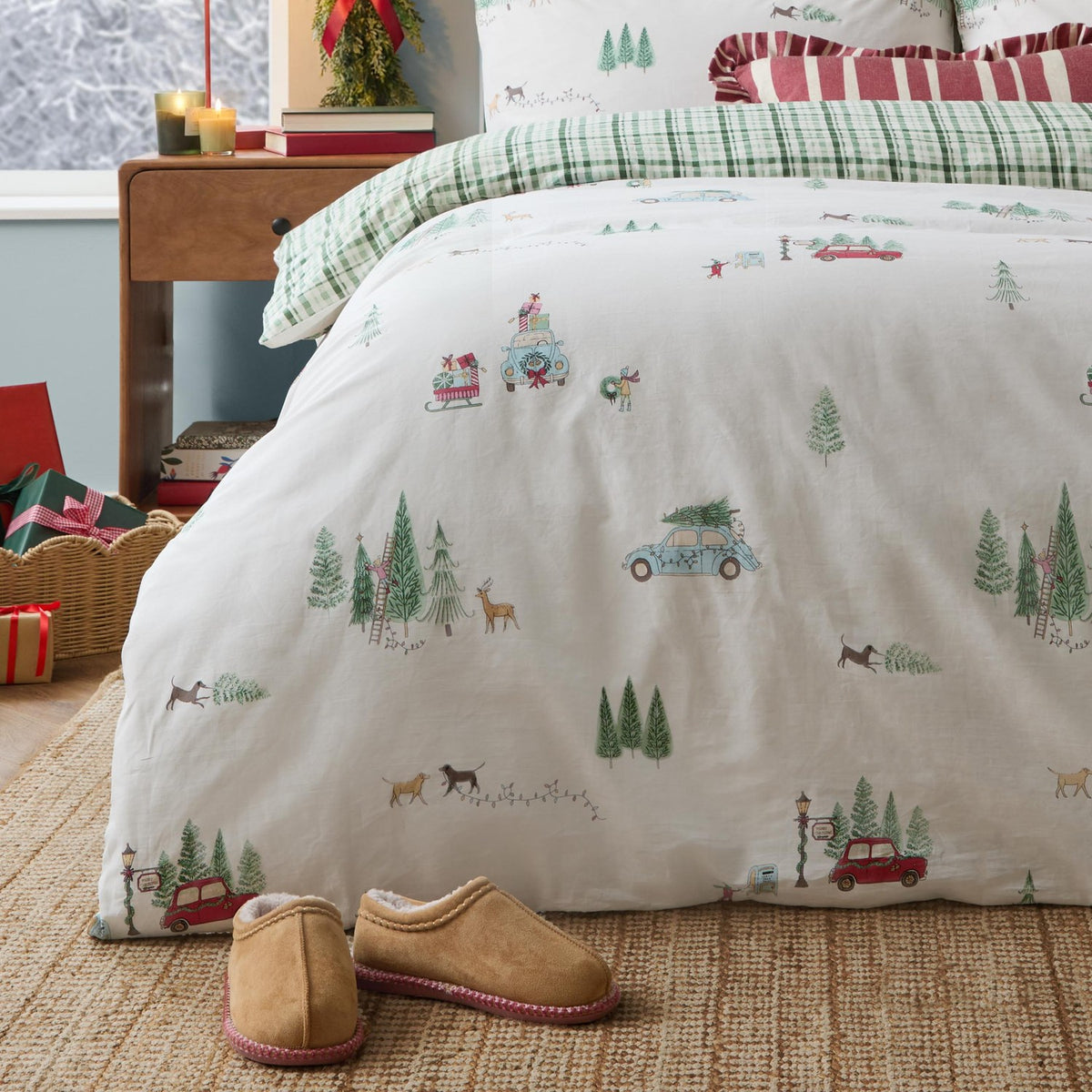 Christmas Tree Lane Check Duvet Cover Set in natural/sage, cotton bedding printed with cars, trees, sleds and deer, reverse green check, styled on a bed with tartan pillowcases and slippers nearby.