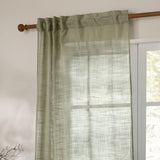 Cirrus sheer curtain panel in eucalyptus green polyester with a slubbed, cross-hatched weave, hung by hidden tab top loops on a wooden pole beside a window.