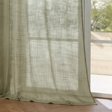 Cirrus Plain Polyester Curtain Panel in Eucalyptus, a sheer green curtain with a slubbed, cross-hatched weave, hanging beside a window with natural light and a wooden floor.