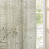 Cirrus Plain Polyester Curtain Panel in Eucalyptus, a sheer green cross-hatched fabric hanging beside a window with soft daylight and greenery visible outside.
