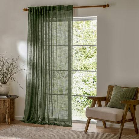 Cirrus Plain Polyester Curtain Panel in forest green, sheer woven fabric with tab-top heading on a wooden rod, hung beside a window in a living room.