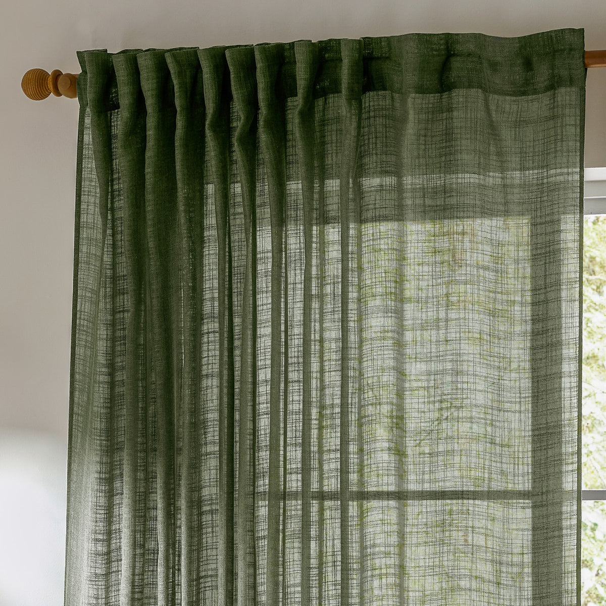 Cirrus Plain Polyester Curtain Panel in forest green, sheer slubbed-weave fabric with tab-top heading on a wooden pole, hung at a window in a bright room.