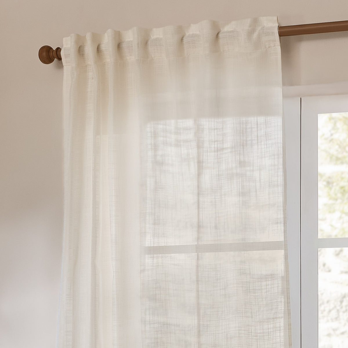 Cirrus Plain Polyester Curtain Panel in pearl cream, sheer woven fabric with tab-top heading on a wooden rod beside a window in a living room.