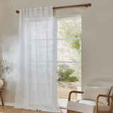 Cirrus Plain Polyester Curtain Panel in snow white sheer fabric, hung on a wooden rod beside a glass door in a living room with an armchair.