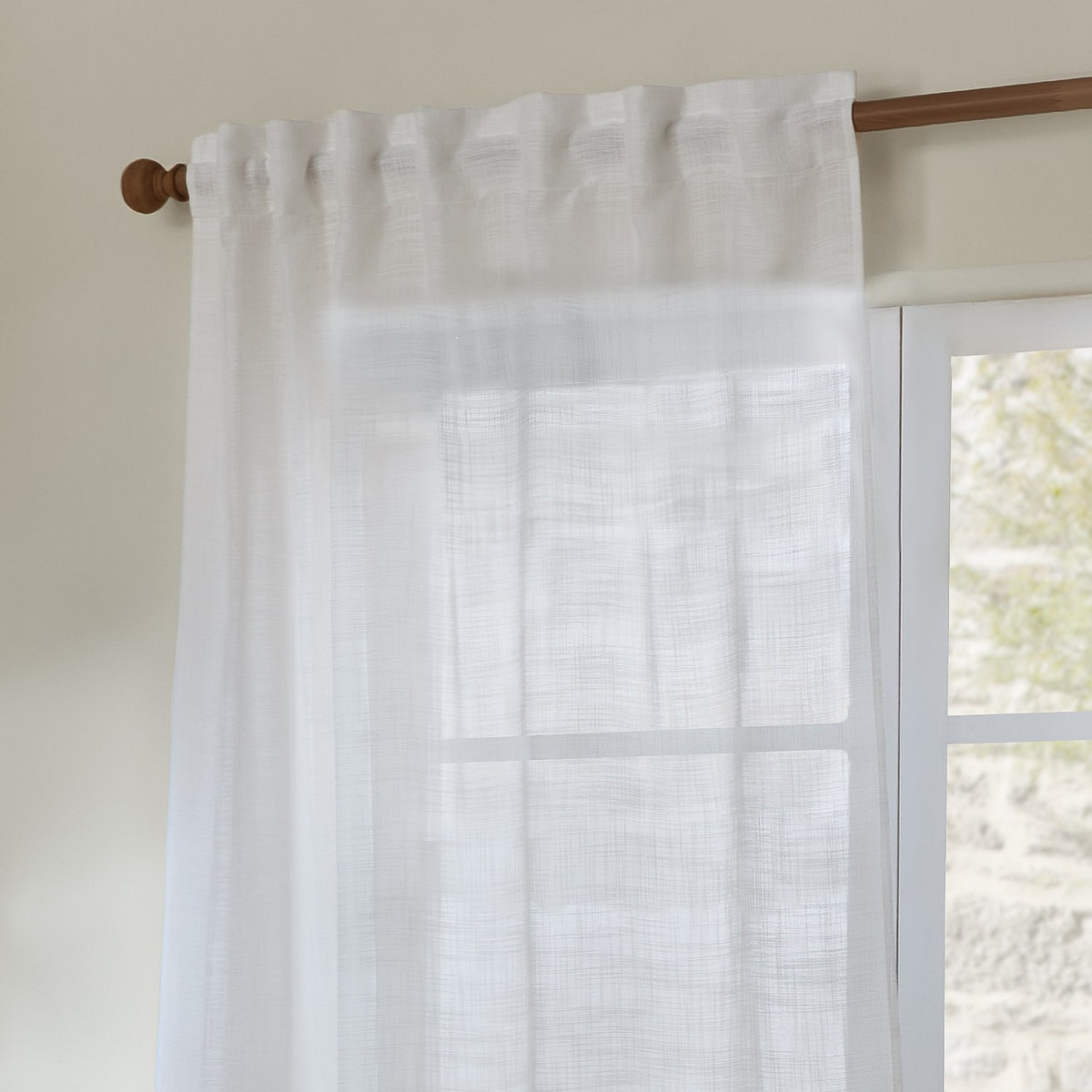 Cirrus Plain Polyester Curtain Panel in snow white, sheer woven fabric with tab-top heading on a wooden rod beside a window in a neutral room.