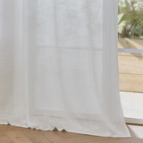Cirrus Plain Polyester Curtain Panel in snow white, a sheer woven fabric panel hanging by a window with visible textured weave, shown in a bright room with wooden flooring.