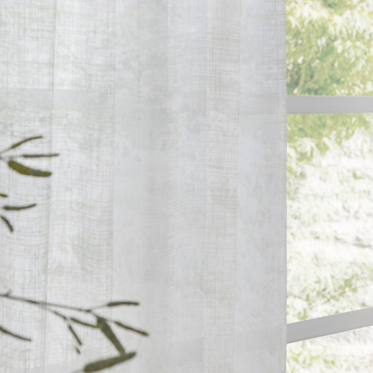 Cirrus Plain Polyester Curtain Panel in snow white, sheer woven fabric with subtle texture, hung beside a window with a leafy outdoor view.