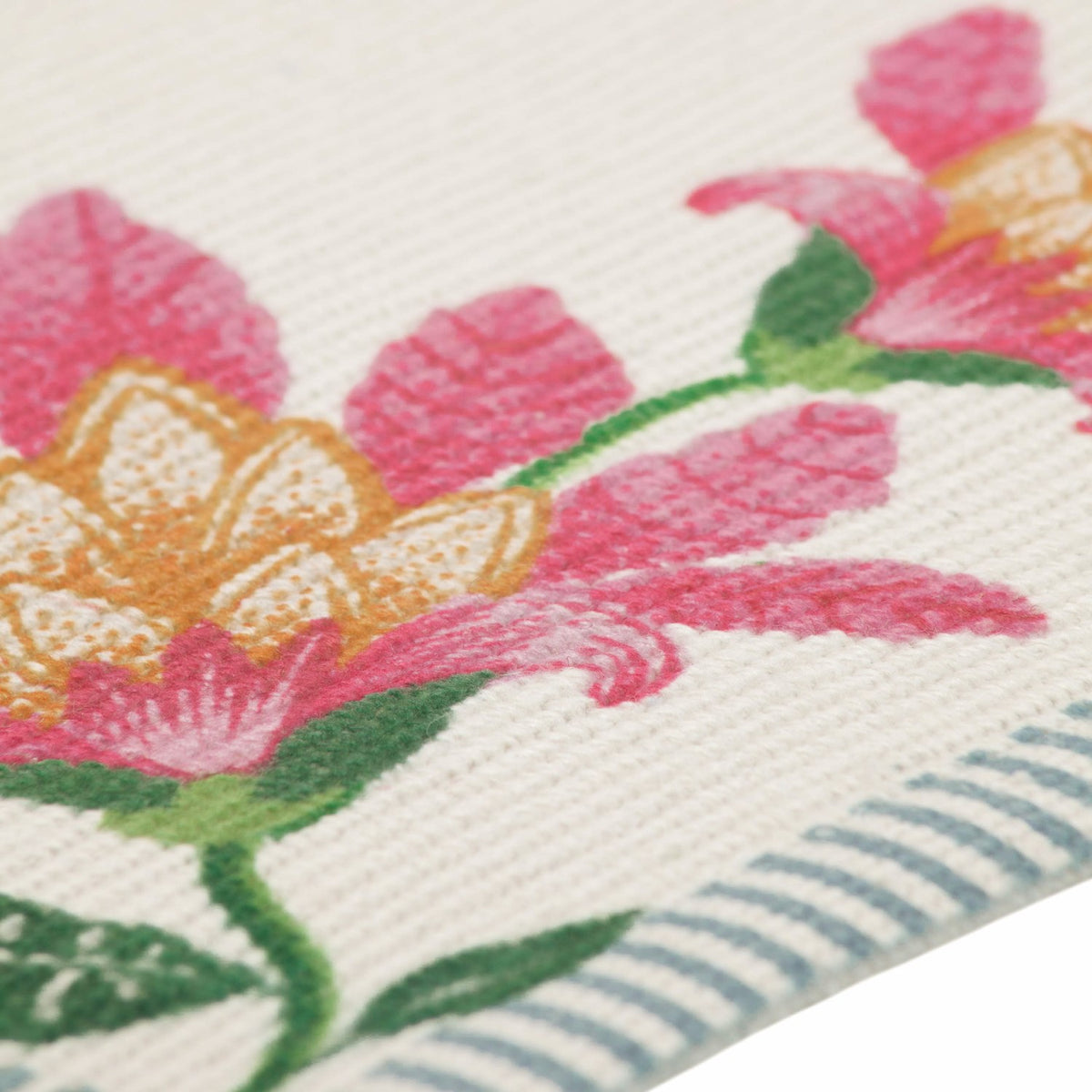 Close-up of the Claudia Floral placemat in polyester, showing pink and amber blooms with green leaves on a cream ribbed weave, edged with a blue and white ticking stripe border.