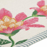 Close-up of the Claudia Floral placemat in polyester, showing pink and amber blooms with green leaves on a cream ribbed weave, edged with a blue and white ticking stripe border.