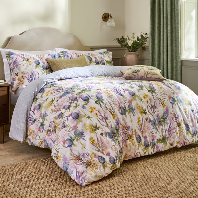 Cluaran Cotton Floral Duvet Cover Set in multi on a bed with matching pillowcases, featuring a watercolour thistle, lavender and floral print in a bedroom setting.