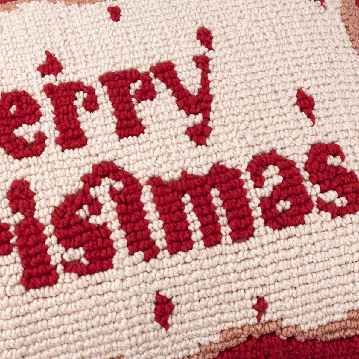 Close-up of the Candy Merry Christmas Tufted Cotton Cushion, showing red hand-hooked "Merry Christmas" script on a cream ground with a red and pink wiggly border.