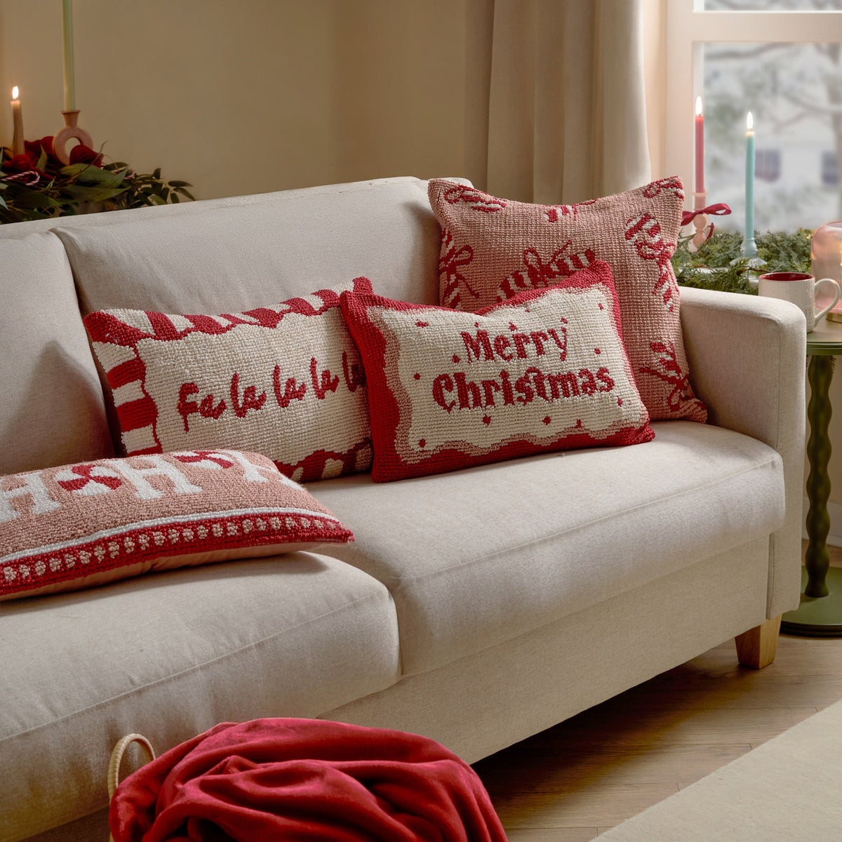 Rectangular tufted cushion with "Merry Christmas" red script on cream, wavy red border, styled among festive cushions on a cream sofa.