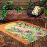 Cockatoo Reversible Polyester Cushion in multicolour with orange trim, shown on a matching patterned rug beside a black woven chair on an outdoor wooden deck.