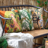 Cockatoo Reversible Polyester Cushion in multicolour with lime-green ground and rust border, shown on an outdoor bench beside leaf-print cushions and a cream throw.