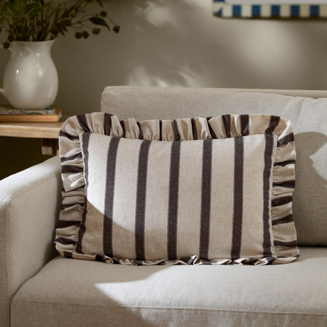 Connie Striped Linen Cushion in chocolate-brown and oatmeal, a rectangular ruffle-edged lumbar cushion resting on a beige sofa in a living room setting.