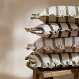 Connie Striped Linen Cushion in Chocolate, second from top of a stacked pile, oatmeal linen with brown stripes and a ruffled edge trim.