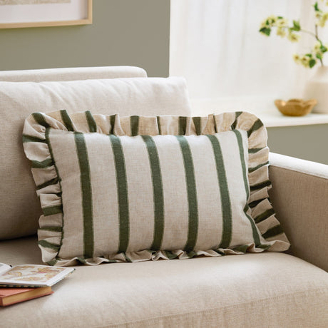 Connie Striped Linen Cushion in Moss, a rectangular cushion with moss green vertical stripes on natural oatmeal linen and a ruffled edge trim, shown on a beige sofa.