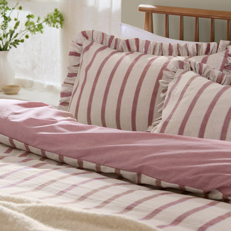 Connie Linen Duvet Cover Set in Clay Pink, shown reversible with striped cream and pink ruffled pillowcases against a plain pink duvet side, styled on a bed in a bedroom setting.