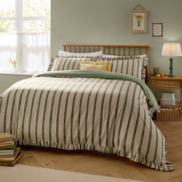 Connie Linen Plain Duvet Cover Set in Moss, shown with green striped duvet cover and matching ruffled pillowcases on a bed, styled in a green-walled bedroom with wooden furniture.