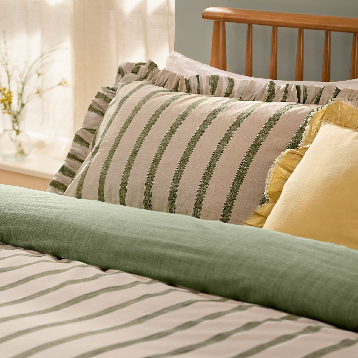 Connie Linen Plain Duvet Cover Set in Moss shown reversible, with green striped pillowcases and plain moss green duvet edge against striped bedding, in a bedroom setting.