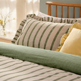 Connie Linen Plain Duvet Cover Set in Moss shown reversible, with green striped pillowcases and plain moss green duvet edge against striped bedding, in a bedroom setting.