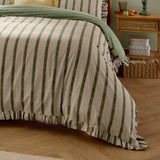 Connie Linen Plain Duvet Cover Set in Moss, striped green and neutral cotton-blend bedding with ruffled edge shown reversed with a plain green throw on a bedroom bed.