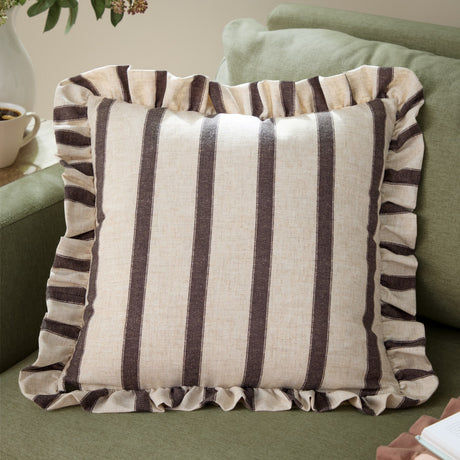 Connie Striped Linen Cushion in Chocolate, a square cream cushion with broad brown stripes and a gathered ruffled edge, shown on a green sofa.