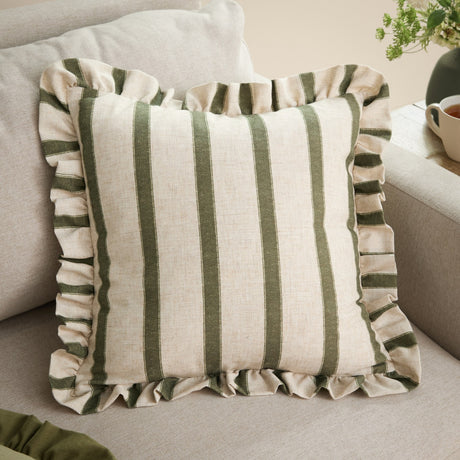 Connie Striped Linen Cushion in Moss, a 45 x 45cm square cushion with vertical moss green stripes on a natural oatmeal linen-look weave and a gathered frilled edge, shown on a beige sofa.