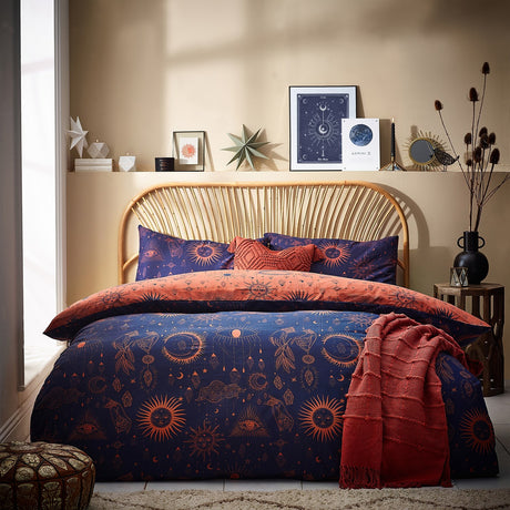 Constellation Printed Reversible Duvet Cover Set in navy with bronze celestial sun, moon and star motifs, styled on a bed with matching pillowcases and a rust throw in a bedroom setting.