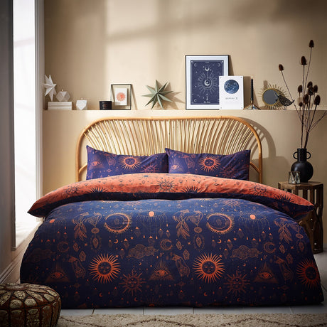 Constellation Printed Reversible Duvet Cover Set in navy and bronze with celestial sun, moon and eye motifs, shown on a bed with matching pillowcases in a bedroom setting.
