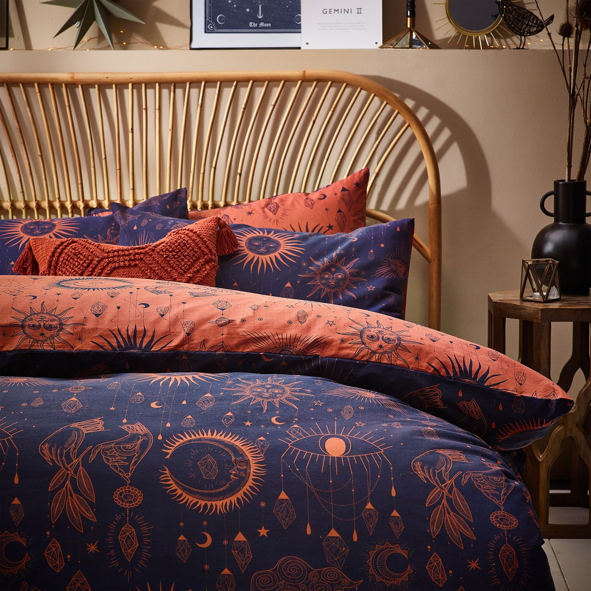 Bronze/Navy Constellation Printed Reversible Duvet Cover Set with celestial sun, moon and star motifs on a bed with rattan headboard, styled with matching pillowcases.