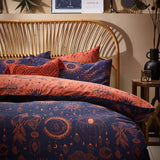 Bronze/Navy Constellation Printed Reversible Duvet Cover Set with celestial sun, moon and star motifs on a bed with rattan headboard, styled with matching pillowcases.